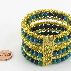 May include: A gold wire wrapped bracelet with multiple rows of turquoise blue beads. The bracelet is about the size of a US penny.