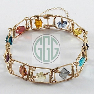 May include: A gold wire bracelet with colorful glass beads. The beads are in various shapes and sizes, including squares, rectangles, and ovals. The bracelet is made of fine wire and has a delicate, feminine look.