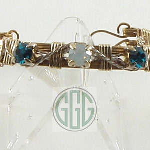 May include: A gold wire wrapped bracelet with three stones. The center stone is a white opal and the two outer stones are teal blue.