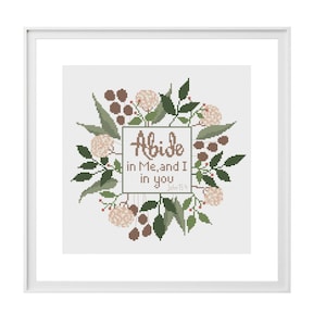 May include: A framed cross stitch pattern with the words "Abide in Me, and I in you" surrounded by a floral wreath. The design features green leaves, brown berries, and pink flowers. The words "PDF pattern" and "cross stitch" are also visible.