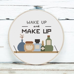 Könnte beinhalten: Gestickte Hoop-Kunst mit dem Text "Wake Up and Make Up" und einem Regal mit einer Vase, einem Glas, einer Flasche und einem Parfümflakon.