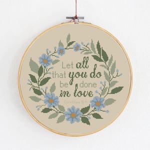 May include: Cross stitch pattern featuring a floral wreath and the text "Let all that you do be done in love, Corinthians 16:14".