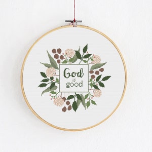 Könnte beinhalten: Ein weißer Stickrahmen mit einem Blumendesign und dem Text "God is good" in grüner Schrift.