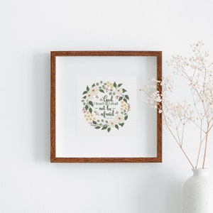 May include: A framed print with a brown wooden frame. The print features a floral wreath design with white flowers, green leaves, and the text "in God I trust I shall not be afraid". A white vase with flowers is in the background.