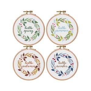 May include: Four embroidery hoops with floral wreaths and the words "hello spring", "hello summer", "hello autumn", and "hello winter".