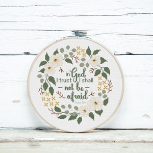 May include: A cross-stitch embroidery hoop featuring the quote "in God I trust I shall not be afraid" surrounded by a floral wreath. The design includes white flowers, green leaves, and yellow accents. Psalm 56:4 is also included.