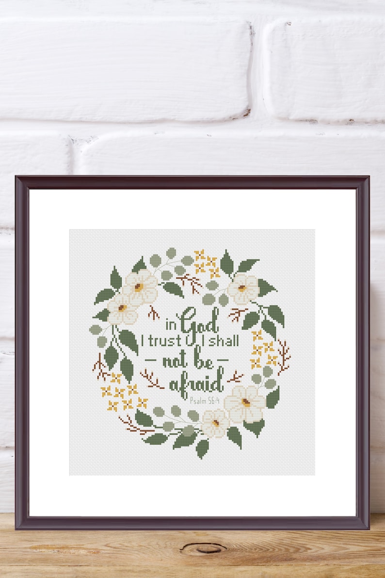 May include: A framed cross-stitch artwork featuring a floral wreath design. The wreath surrounds the text "in God I trust I shall - not be - afraid" from Psalm 56:4. The design includes white flowers, green leaves, and yellow accents.