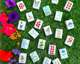 Puede incluir: Un conjunto de fichas de mahjong rectangulares blancas con ilustraciones coloridas de elementos de jardín, incluyendo fresas, zanahorias, mariposas, flores, un gnomo de jardín, un invernadero y herramientas, con etiquetas north, south, east, west y joker.