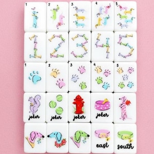 May include: A set of white Mahjong tiles with colorful illustrations. The tiles feature numbers, paw prints, dachshunds, and other dog-themed images. Some tiles have the word "joker", and others have "east" and "south".