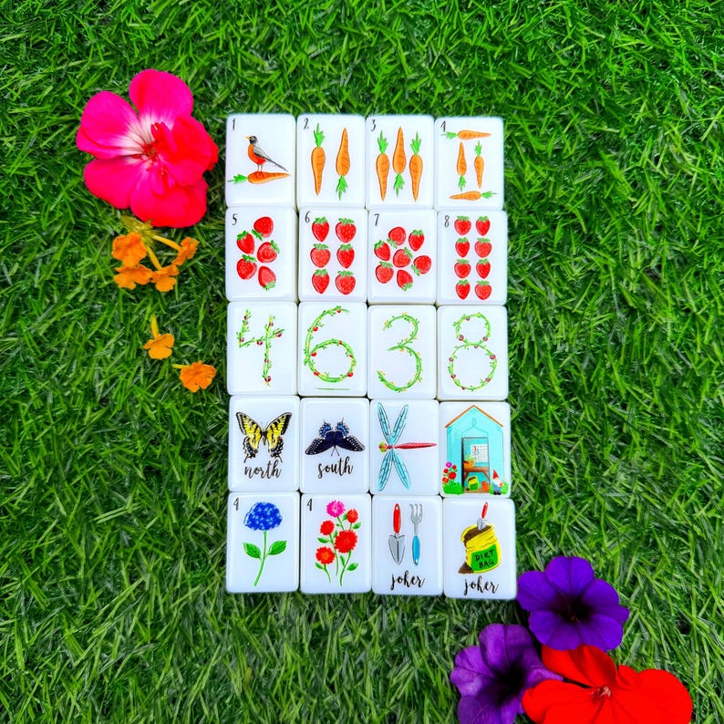 Pode incluir: Um conjunto de vinte pe&ccedil;as retangulares brancas de mahjong dispostas numa grelha, com ilustra&ccedil;&otilde;es coloridas de p&aacute;ssaros, cenouras, morangos, borboletas, ferramentas de jardim e n&uacute;meros formados por videiras, com o texto north, south, joker.