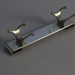 May include: A silver metal hook rack with two hooks. The rack is designed to be mounted on a wall.