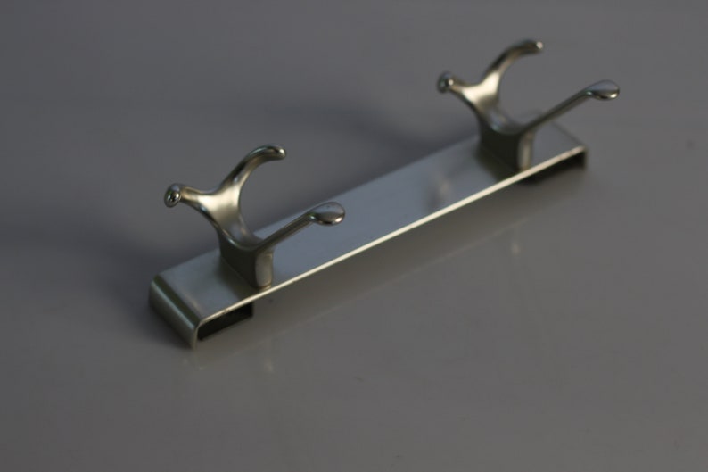 May include: A silver metal hook rack with two hooks. The rack is designed to be mounted on a wall.