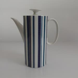 Op de afbeelding: Witte keramische koffiekan met een blauw en paars gestreept ontwerp. De kan heeft een deksel en een handvat.