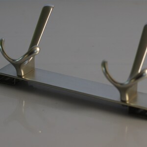 May include: A silver metal hook rack with two hooks. The rack is rectangular and has a smooth, polished finish.