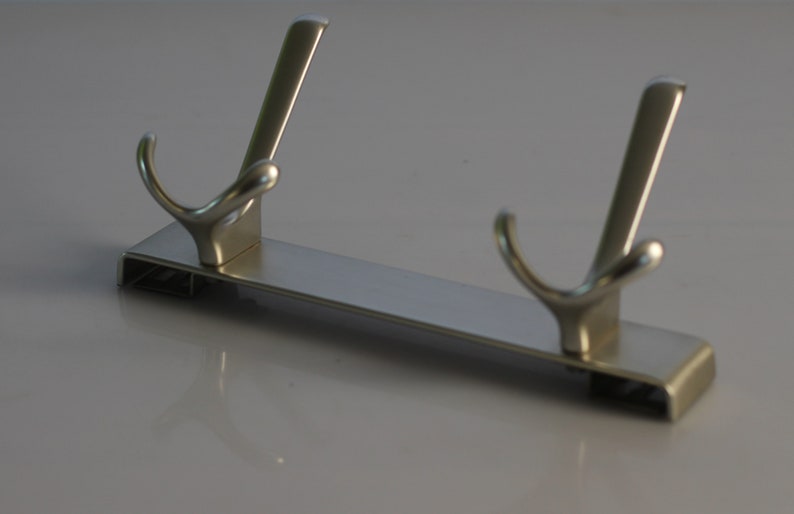 May include: A silver metal hook rack with two hooks. The rack is rectangular and has a smooth, polished finish.