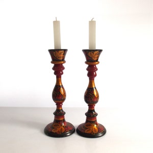 May include: A pair of black, red, and gold painted wooden candle holders with white candles. The candle holders have a floral design.