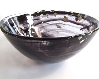 May include: A large, black glass bowl with white and silver swirls and flecks. The bowl has a Kosta Boda logo on the bottom.