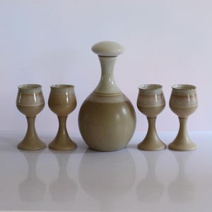 May include: A set of five ceramic pieces, including a decanter and four goblets. The decanter has a white lid and a brown and white glaze. The goblets are all brown and white.