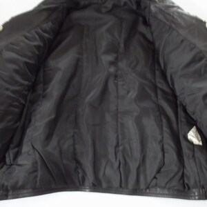 May include: Black leather jacket with silver-tone stud embellishments on the shoulders. The interior is lined with black satin fabric. The jacket is open, revealing the inside lining and construction.