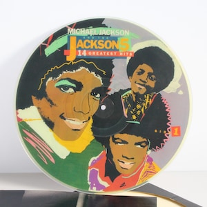 May include: A vintage vinyl record featuring the album "14 Greatest Hits" by Michael Jackson and The Jackson 5. The album cover art showcases colorful illustrations of Michael Jackson and his brothers, with text in green, red, and yellow.