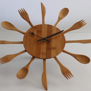 May include: A wooden clock with a round, brown face and black hands. The clock is made of wooden utensils, including forks, spoons, and knives, arranged in a circular pattern.