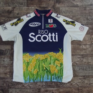 May include: White and blue cycling jersey with a large RISO SCOTTI logo and a design of rice plants. The jersey has several sponsor logos including PLAYBUS, AREO, MOG, and FILA.