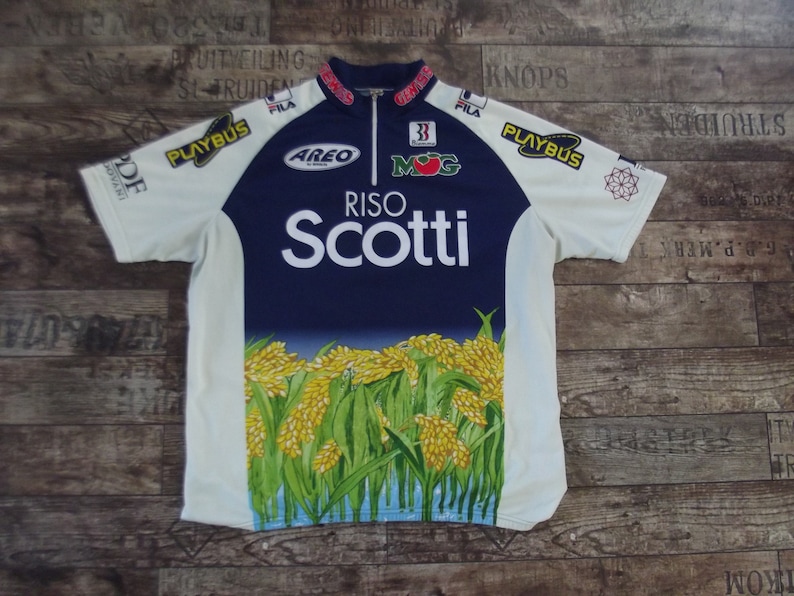 May include: White and blue cycling jersey with a large RISO SCOTTI logo and a design of rice plants. The jersey has several sponsor logos including PLAYBUS, AREO, MOG, and FILA.
