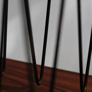 Puede incluir: Primer plano de patas de horquilla de metal negro sobre una superficie de madera. Las patas est&aacute;n inclinadas y forman una V.