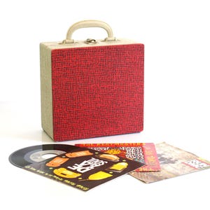 Puede incluir: Un estuche rojo y beige para discos de vinilo con asa crema. Varios discos de vinilo y portadas de álbumes están frente al estuche, incluido uno que dice "The Beatmasters".