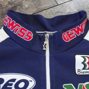 May include: A blue and white cycling jersey with red "GEWISS" text on the collar, a white zipper, and a white "Biemme" logo with a green, white, and red stripe design.