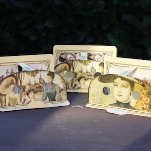 May include: Several vintage-style photo holders with sepia-toned images of women and landscapes. The holders are rectangular with arched fronts, featuring cut-out circles and decorative borders. The overall aesthetic is antique and nostalgic.