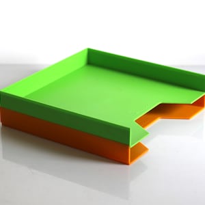 May include: A green and orange plastic desk organiser with two compartments. The organiser is made of durable plastic and is ideal for organising papers, pens, and other office supplies.