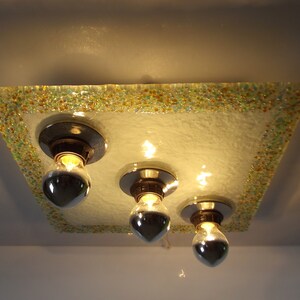 May include: A square ceiling light fixture with a frosted glass shade. The shade has a decorative border of small, colorful glass beads. The light fixture has three exposed bulbs.