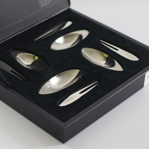 May include: A black box with a velvet interior holds a set of six silver spoons and forks. The box is labeled "GENEVA Stainless"
