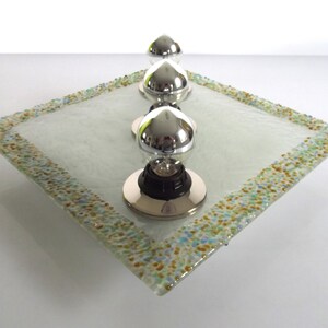 May include: Three silver lightbulb fixtures on a square glass tray with a speckled border. The tray is white with a frosted finish.