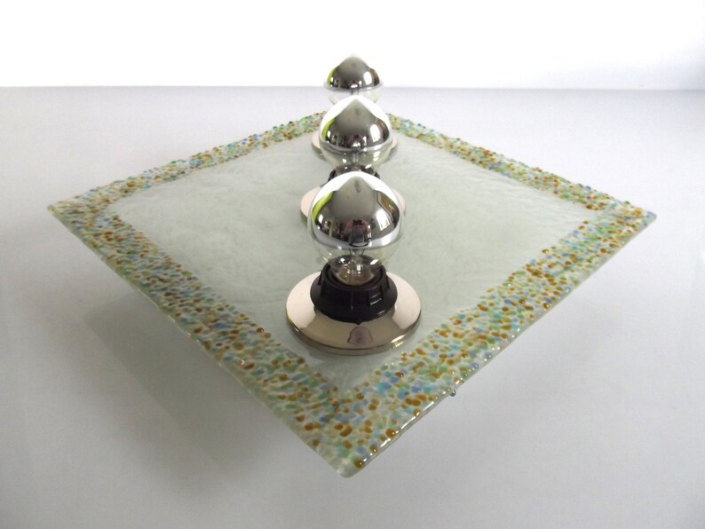 May include: Three silver lightbulb fixtures on a square glass tray with a speckled border. The tray is white with a frosted finish.