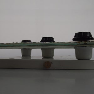 May include: Three black knobs on a white ceramic base with a clear glass top. The knobs are mounted on white ceramic posts.