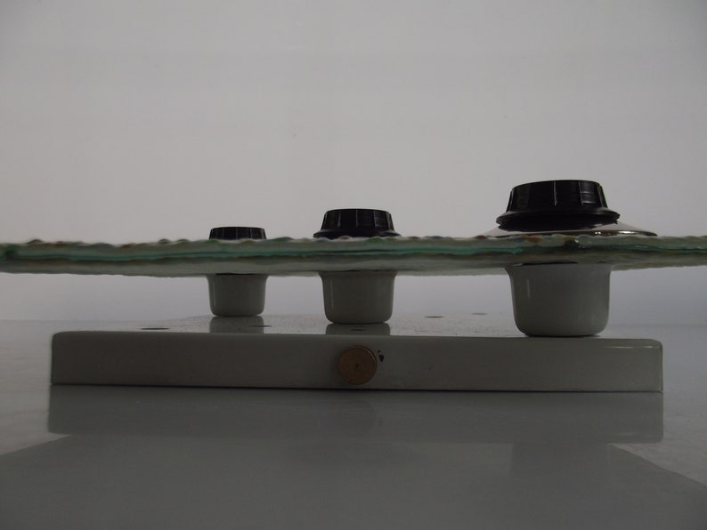 May include: Three black knobs on a white ceramic base with a clear glass top. The knobs are mounted on white ceramic posts.