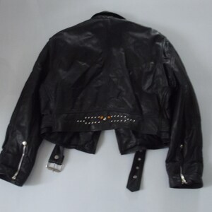 May include: Black leather jacket with silver zippers on the sleeves and a studded design across the back. The jacket has a notched collar, a belt with a silver buckle, and a cropped waist.