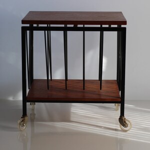 Puede incluir: Un soporte para discos de metal negro con una tapa de madera y ruedas. El soporte tiene una forma rectangular y est&aacute; dise&ntilde;ado para sostener discos verticalmente.