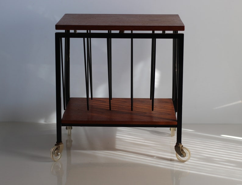 Puede incluir: Un soporte para discos de metal negro con una tapa de madera y ruedas. El soporte tiene una forma rectangular y est&aacute; dise&ntilde;ado para sostener discos verticalmente.