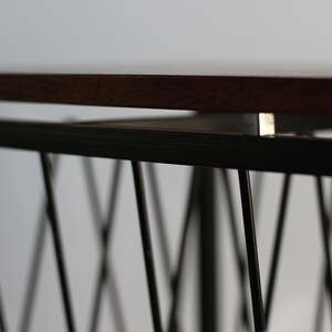Puede incluir: Una mesa de madera con un marco de metal negro. El marco tiene un dise&ntilde;o geom&eacute;trico con una serie de l&iacute;neas que se cruzan.
