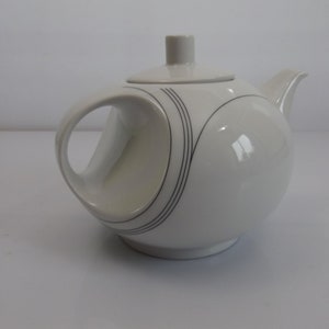 Può includere: Teiera in ceramica bianca con un design astratto in bianco e nero. La teiera ha un'impugnatura unica e un coperchio.