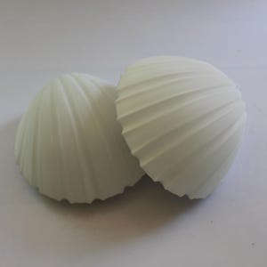 Op de afbeelding: Twee matwitte, halfronde objecten met een duidelijke geribbelde, geschulpte textuur die vanuit het midden naar de buitenranden straalt. Deze koepelvormige items hebben een uniforme, effen kleur en een gladde, consistente afwerking.