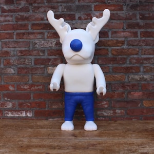 Puede incluir: Una figura antropomórfica blanca con grandes astas y una nariz azul prominente. La figura tiene un acabado mate liso, brazos y torso blancos, y viste pantalones azules. Se mantiene en posición vertical con brazos y manos articulados.