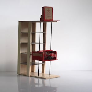 May include: A vintage toy garage with a red and white race car inside. The garage has multiple shelves and a sign that reads "Simplex Token Garage". The structure is made of wood and metal.