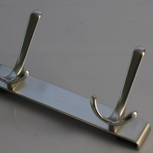 May include: A silver metal hook rack with two double hooks. The rack is designed to be mounted on a wall.