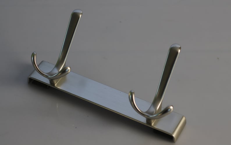May include: A silver metal hook rack with two double hooks. The rack is designed to be mounted on a wall.