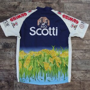 May include: A white cycling jersey with blue and yellow accents. The jersey features the text "Scotti" and "Riso" on the front, along with a graphic of rice plants. The sleeves have the text "Gewiss" on them.
