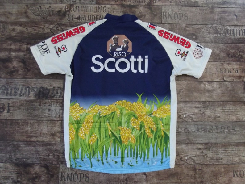 May include: A white cycling jersey with blue and yellow accents. The jersey features the text "Scotti" and "Riso" on the front, along with a graphic of rice plants. The sleeves have the text "Gewiss" on them.